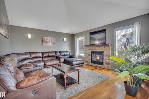 Living room featuring hardwood floors, a stone fireplace, and vaulted ceilings - 316 Avena Link, Leduc, AB - Indoor Photo Showing Living Room With Fireplace
