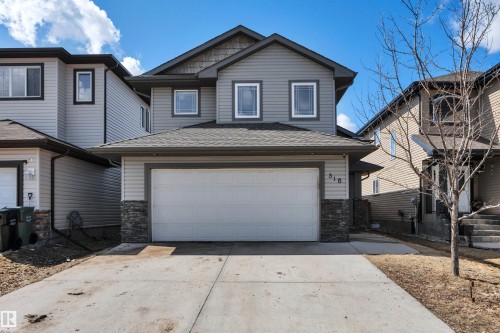 The property features a two-story design with gray siding and stone accents, a double garage, and a paved driveway - 316 Avena Link, Leduc, AB - Outdoor With Facade