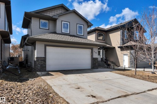 The property features a two-story exterior with grey siding and stone detailing, a two-car garage, and a concrete driveway - 316 Avena Link, Leduc, AB - Outdoor With Facade