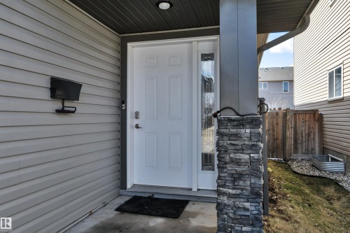 The property features a white paneled front door with a decorative glass sidelight, complemented by a stone-clad pillar - 316 Avena Link, Leduc, AB - Outdoor With Exterior