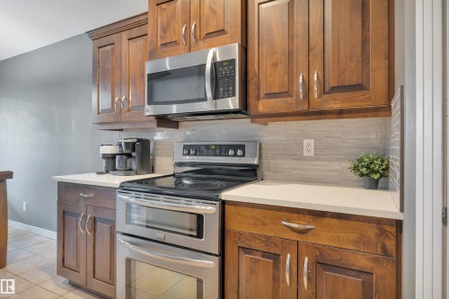 The kitchen features wooden cabinetry, stainless steel appliances, light-toned countertops, and a tiled backsplash - 316 Avena Link, Leduc, AB - Indoor Photo Showing Kitchen