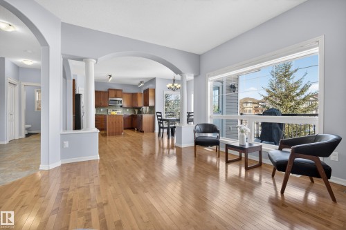 This living area features light hardwood flooring, a large window providing views of outdoor trees and properties, and arched doorways - 20714 56A Avenue, Edmonton, AB - Indoor Photo Showing Other Room