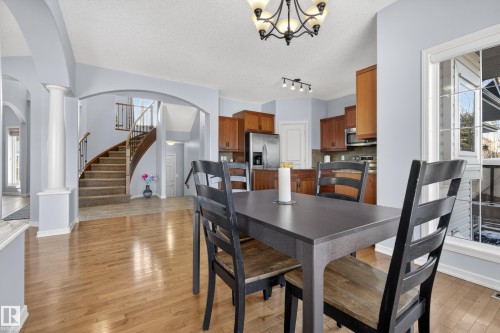 This inviting interior features light hardwood flooring, light blue wall paint, and a classic chandelier - 20714 56A Avenue, Edmonton, AB - Indoor Photo Showing Dining Room