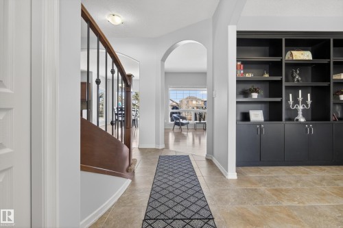 The entrance foyer features tile flooring, a built-in shelving unit with lower cabinetry, and an arched doorway leading to another living space - 20714 56A Avenue, Edmonton, AB - Indoor Photo Showing Other Room