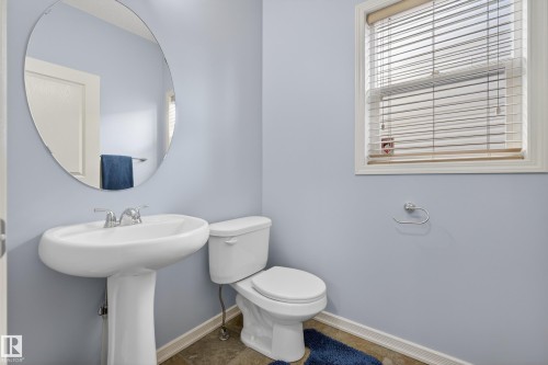 Bathroom featuring a pedestal sink with a chrome faucet, a white toilet, and an oval mirror - 20714 56A Avenue, Edmonton, AB - Indoor Photo Showing Bathroom