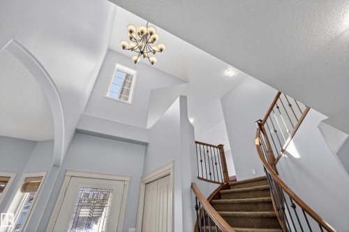 The property features a grand entrance with a high ceiling, a large decorative chandelier, and a curved staircase with wooden handrails and wrought iron balusters - 20714 56A Avenue, Edmonton, AB - Indoor Photo Showing Other Room