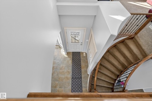 The property features a staircase with carpeted treads and wood and wrought iron railings, leading to a tiled entry area with a white front door - 20714 56A Avenue, Edmonton, AB - Indoor Photo Showing Other Room