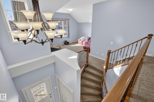 Foyer and upper level living area featuring a decorative chandelier, a staircase with wooden handrails and metal balusters, and a front entry door with decorative glass inserts - 20714 56A Avenue, Edmonton, AB - Indoor Photo Showing Other Room