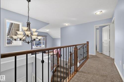 Upper landing with carpeted flooring, light blue walls, and a view of the staircase featuring a dark wood handrail and black metal balusters - 20714 56A Avenue, Edmonton, AB - Indoor Photo Showing Other Room