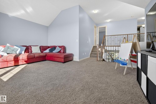 Spacious carpeted area with a vaulted ceiling and light blue walls, featuring a staircase with a wooden handrail and black metal balusters - 20714 56A Avenue, Edmonton, AB - Indoor