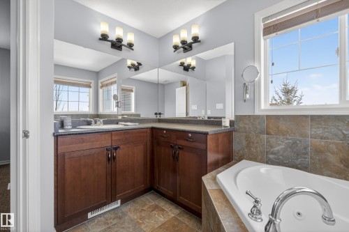 The bathroom features a corner soaking tub, a double vanity with ample storage, and two windows providing natural light - 20714 56A Avenue, Edmonton, AB - Indoor Photo Showing Bathroom