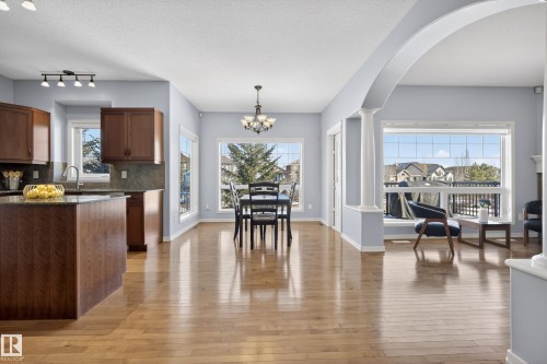 This property features an open-concept layout with hardwood floors throughout, a kitchen with dark wood cabinetry and a central island, and a dining area illuminated by a chandelier - 20714 56A Avenue, Edmonton, AB - Indoor