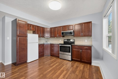 The kitchen features wood cabinetry, a stainless steel range and microwave, a white refrigerator, and a window providing natural light - 20714 56A Avenue, Edmonton, AB - Indoor Photo Showing Kitchen