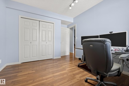 Room featuring light blue walls, wood-look flooring, and white bi-fold closet doors - 20714 56A Avenue, Edmonton, AB - Indoor Photo Showing Office