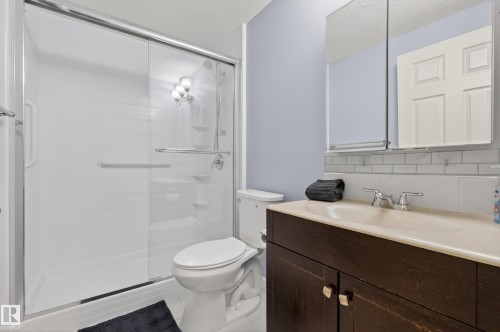 Bathroom featuring a shower with glass doors, a vanity with a light-colored countertop and dark wood cabinetry, and a mirrored medicine cabinet above the vanity - 20714 56A Avenue, Edmonton, AB - Indoor Photo Showing Bathroom