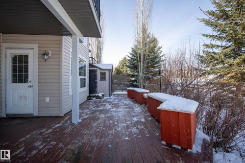 The property features a wooden deck with red planters and a built-in storage shed, set against a backdrop of mature trees - 20714 56A Avenue, Edmonton, AB - Outdoor With Exterior