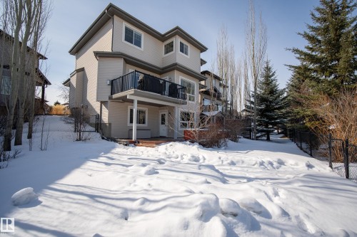 The property features a two-story exterior with light-colored siding, a balcony with a black railing, and a ground-level patio area - 20714 56A Avenue, Edmonton, AB - Outdoor