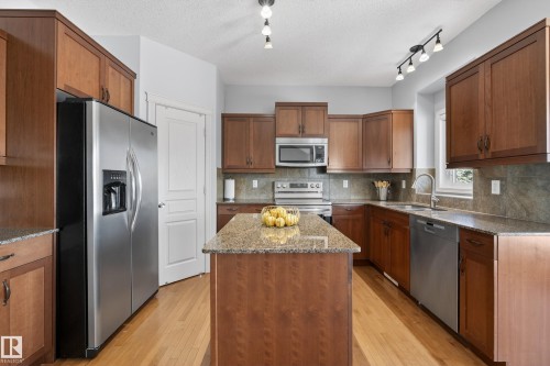 The kitchen features extensive wooden cabinetry, stainless steel appliances, a center island with a granite countertop, and light wood flooring - 20714 56A Avenue, Edmonton, AB - Indoor Photo Showing Kitchen With Double Sink