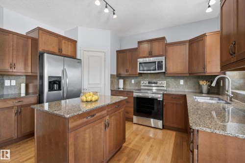 Well-appointed kitchen featuring a center island, granite countertops, wood cabinetry, and stainless steel appliances - 20714 56A Avenue, Edmonton, AB - Indoor Photo Showing Kitchen With Double Sink