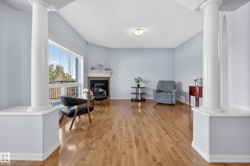 Living area featuring hardwood floors, decorative columns, a fireplace with a mantel, and large windows providing natural light - 20714 56A Avenue, Edmonton, AB - Indoor With Fireplace
