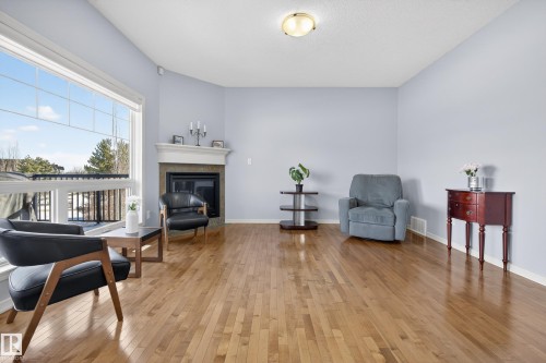 Spacious living area featuring hardwood flooring, a fireplace with a mantel, and large windows providing natural light - 20714 56A Avenue, Edmonton, AB - Indoor Photo Showing Living Room With Fireplace