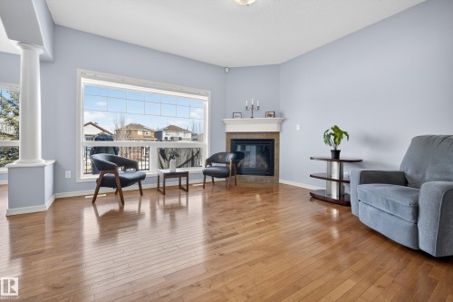 Spacious living area featuring hardwood floors, large windows providing natural light, a corner fireplace with a mantel, and a decorative column - 20714 56A Avenue, Edmonton, AB - Indoor Photo Showing Living Room With Fireplace
