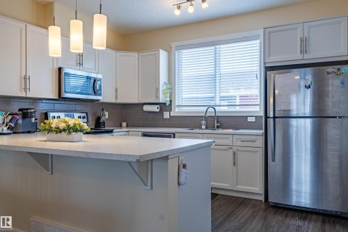 The kitchen features white cabinetry, a gray tile backsplash, and stainless steel appliances, including a microwave and a refrigerator - 2679 Maple Way, Edmonton, AB - Indoor Photo Showing Kitchen With Upgraded Kitchen