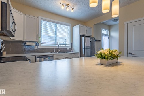 The kitchen features light-colored cabinetry, a window with blinds, stainless steel appliances, and a grey tile backsplash - 2679 Maple Way, Edmonton, AB - Indoor Photo Showing Kitchen