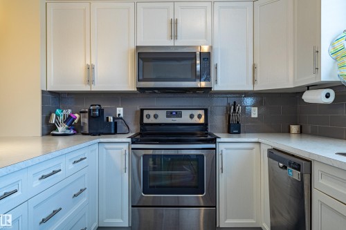 The kitchen features white cabinetry, a grey subway tile backsplash, and stainless steel appliances including a microwave, oven with an electric cooktop, and a dishwasher - 2679 Maple Way, Edmonton, AB - Indoor Photo Showing Kitchen With Stainless Steel Kitchen