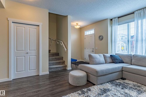 Living room featuring wood-look flooring, a staircase with carpeting, and a bright window with blinds and sheer curtains - 2679 Maple Way, Edmonton, AB - Indoor Photo Showing Living Room