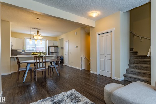 Open concept living space featuring wood-look flooring, a kitchen with white cabinetry and stainless steel appliances, and a carpeted staircase - 2679 Maple Way, Edmonton, AB - Indoor Photo Showing Other Room