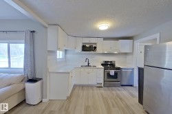 The property features a kitchen with white cabinetry, stainless steel appliances, and light-toned flooring - 
