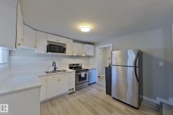 The kitchen features white cabinetry, light-toned countertops, and stainless steel appliances including a refrigerator, stove, and microwave - 