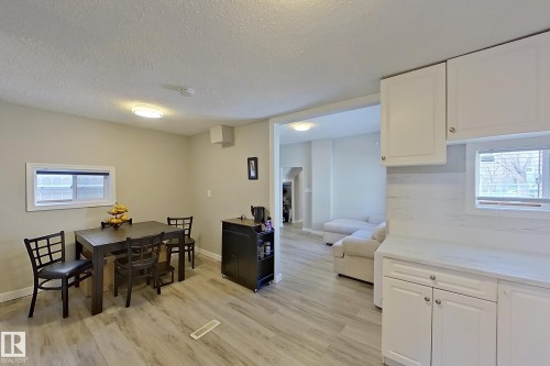 The property features a dining area with wood-look flooring and a window, seamlessly connected to a kitchen area with white cabinetry and a window - 9328 106A Avenue, Edmonton, AB - Indoor