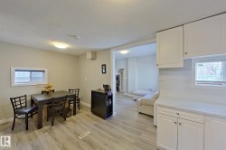 The property features a dining area with wood-look flooring and a window, seamlessly connected to a kitchen area with white cabinetry and a window - 