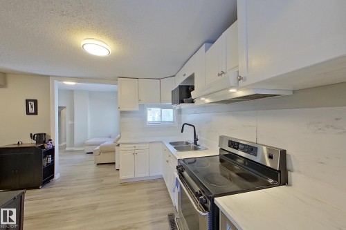 The kitchen features white cabinetry, a double basin sink with a black faucet, and stainless steel appliances - 9328 106A Avenue, Edmonton, AB - Indoor Photo Showing Kitchen With Double Sink