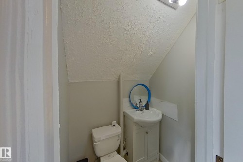 Bathroom featuring a white toilet, a white vanity with a basin sink, and an oval mirror with a blue frame - 9328 106A Avenue, Edmonton, AB - Indoor Photo Showing Bathroom