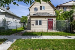 Two-story residence featuring light-toned horizontal siding, a red entry door with a decorative glass insert, and a chain-link fence enclosing the front yard - 