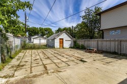 Expansive outdoor space featuring a large concrete patio, perimeter fencing, and a detached storage shed with a wooden door - 