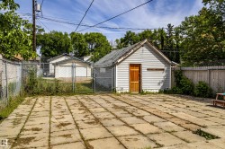 Paved patio area featuring large concrete pavers, a chain-link fence, and a detached white-sided shed with a natural wood door - 