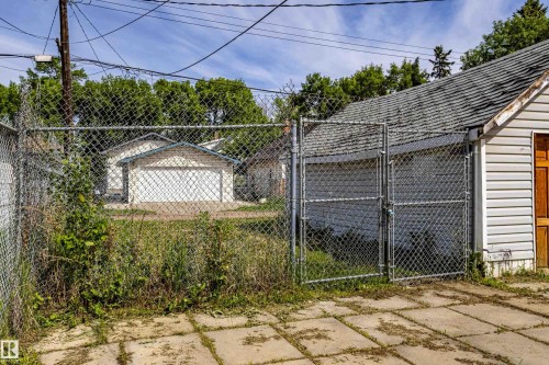 Chain-link fenced yard with concrete slab patio and detached garage featuring horizontal siding and a shingled roof - 9328 106A Avenue, Edmonton, AB 