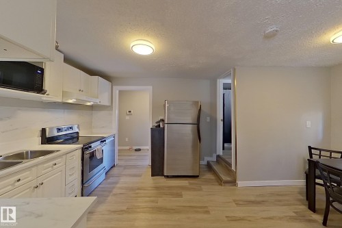 The kitchen features stainless steel appliances, white cabinetry, a double basin sink, and light-toned flooring - 9328 106A Avenue, Edmonton, AB - Indoor Photo Showing Kitchen With Double Sink