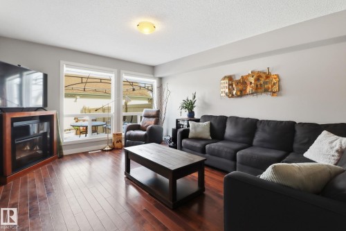 The living area features polished wood flooring, large windows, and a built-in entertainment unit with an electric fireplace - 430 Watt Boulevard, Edmonton, AB - Indoor Photo Showing Living Room With Fireplace