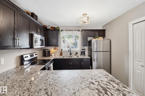 The kitchen features dark wood cabinetry, granite countertops, and stainless steel appliances, including a microwave, refrigerator, and electric range - 430 Watt Boulevard, Edmonton, AB - Indoor Photo Showing Kitchen