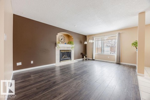 Living area featuring dark wood-look flooring, a fireplace with a tiled surround, and a large window - 7 Doucette Place, St. Albert, AB - Indoor Photo Showing Living Room With Fireplace
