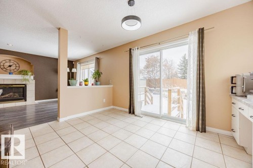 Spacious room with tile flooring, sliding glass doors opening to a snow-covered yard, and a partial view of a fireplace with a mantel in an adjoining room - 7 Doucette Place, St. Albert, AB - Indoor