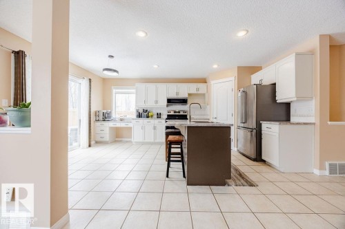 The kitchen features white cabinetry, stainless steel appliances, a center island with a breakfast bar, and tile flooring - 7 Doucette Place, St. Albert, AB - Indoor Photo Showing Kitchen