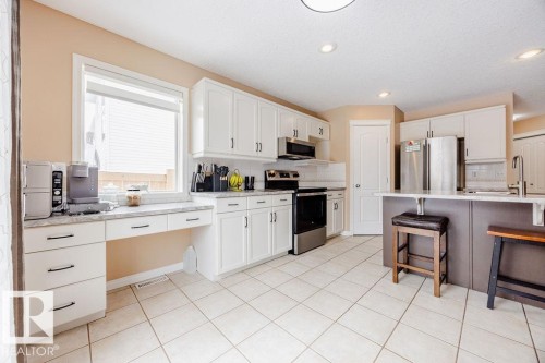 The kitchen features white cabinetry, stainless steel appliances, a center island with seating, and tiled flooring - 7 Doucette Place, St. Albert, AB - Indoor Photo Showing Kitchen