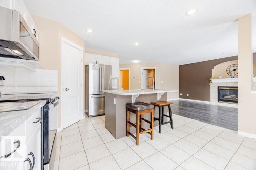 The kitchen features a white tile floor, stainless steel refrigerator, white cabinetry, and an island with seating - 7 Doucette Place, St. Albert, AB - Indoor Photo Showing Kitchen