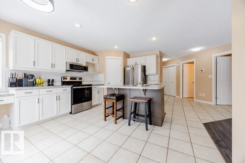 The kitchen features white cabinetry, stainless steel appliances, a breakfast bar, and tile flooring - 7 Doucette Place, St. Albert, AB - Indoor Photo Showing Kitchen
